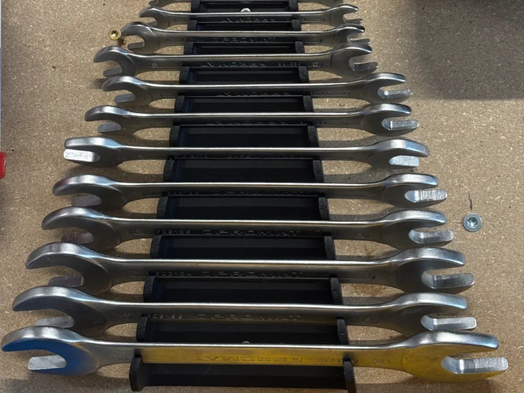 Soportes negros impresos en 3D con un juego de llaves fijas colocadas en fila sobre un tablero de taller
