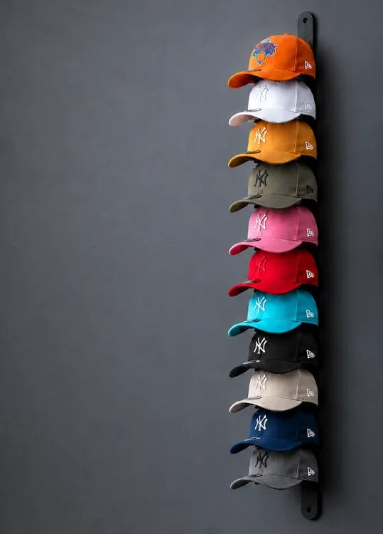 Soporte de pared vertical negro con gorras de colores colgadas una encima de otra